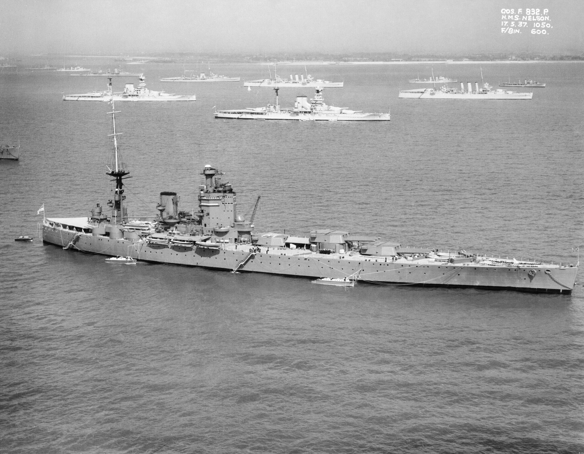 Aerial view of the battleship HMS Nelson at anchor, with two Queen Elizabeth-class battleships and two London-class cruisers anchored beyond her